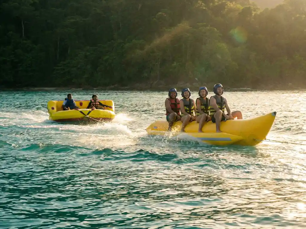 Gele en bananvormige opblaasbare slepen racen over turquoise water met witte kielzog en beboste kustlijn