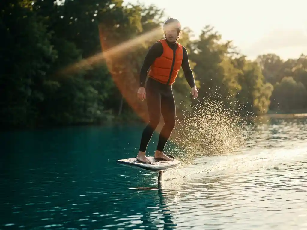 Persoon op e-foil board met oranje impactvest glijdt over kalm blauw water met waterdruppels in zonlicht