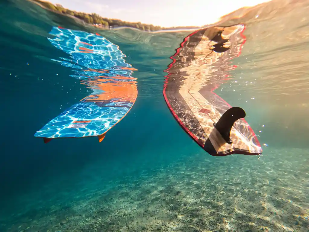 Twee wakeboards verticaal zwevend onder kristalhelder meerwater met zonlicht dat dansende patronen creëert op de glanzende oppervlakken