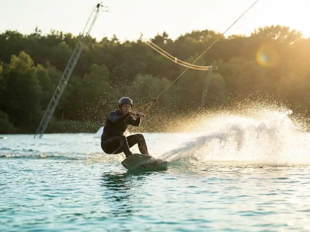 Wakeboarder in perfecte houding tijdens scherpe bocht door turquoise water van Belgisch kabelbaan-meer, omringd door groen bos