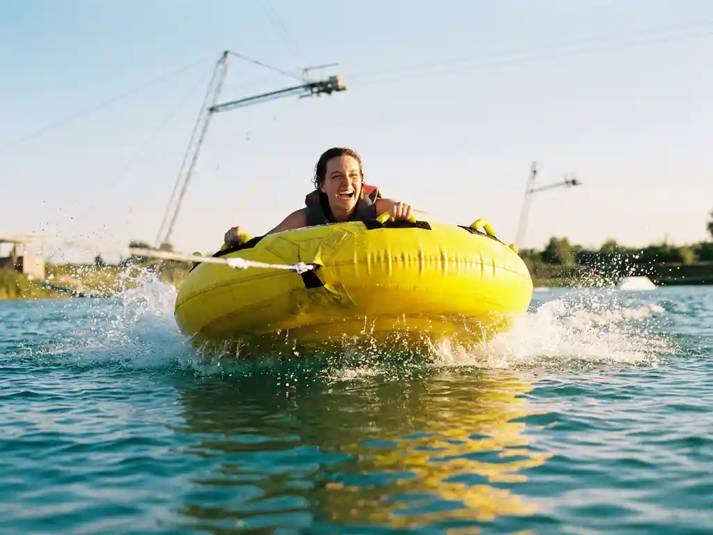 Lachende persoon op gele opblaasbare sleepband met waterspetters op turquoise water in kabelpark