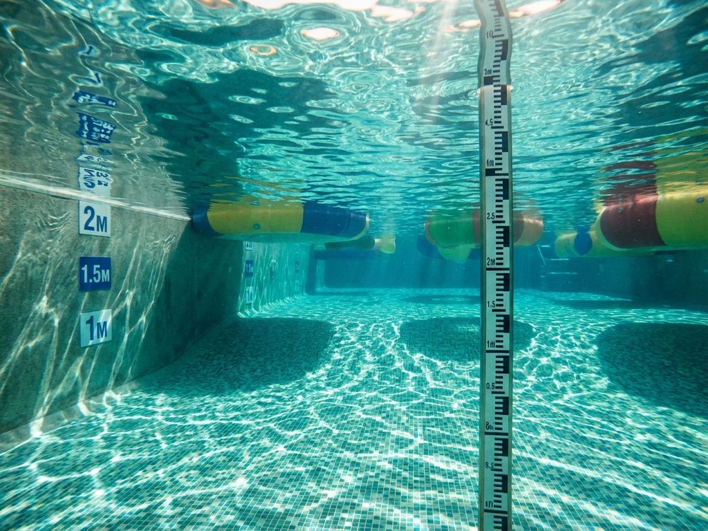 Onderwaterzicht van zwembadbodem met dieptemarkeringen, drijvende obstakels en zonlicht door turquoise water